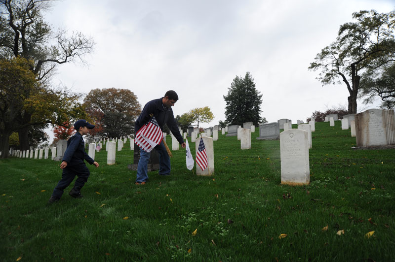 Padre con hijo colocando banderas antes del Día de los Veteranos en el Cementerio Nacional de Arlington - Maneras de honrar a los veteranos cerca de Washington, DC
