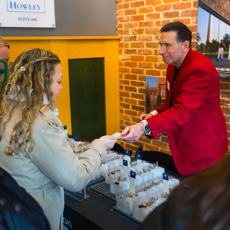A staff member in a red jacket hands a name badge to an attendee at a Destination DC event check-in table lined with organized badges against a brick wall backdrop.