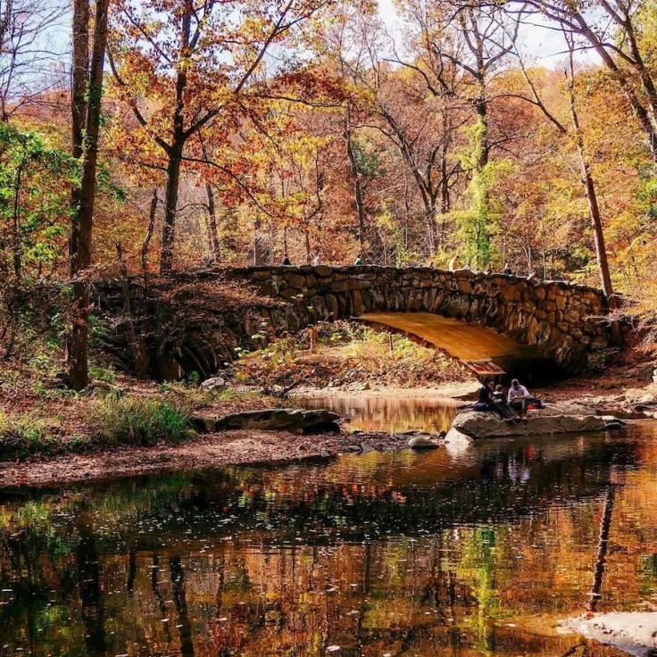 Photo of an arched stone bridge over a calm creek, reflected in autumn trees