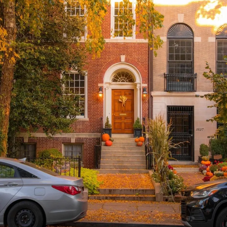 Photo of row house entry with orange door, pumpkins and fall leaves on steps
