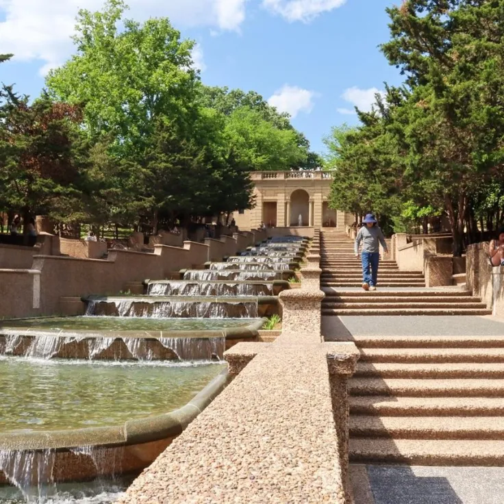 Terraced fountain and steps in a tree-lined plaza under a blue sky