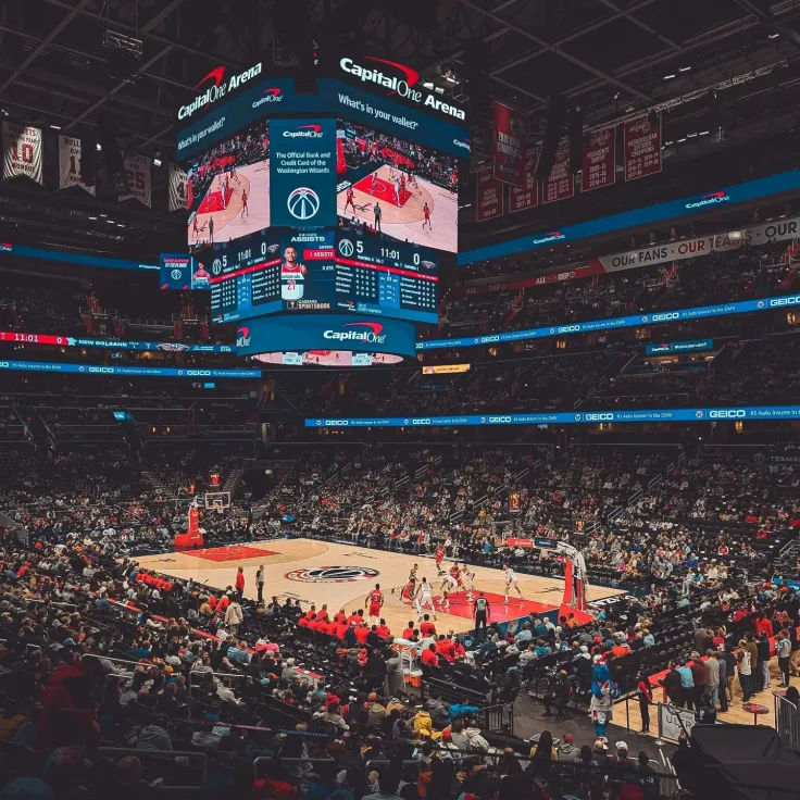 Photo of a packed arena during a basketball game with a large center scoreboard.