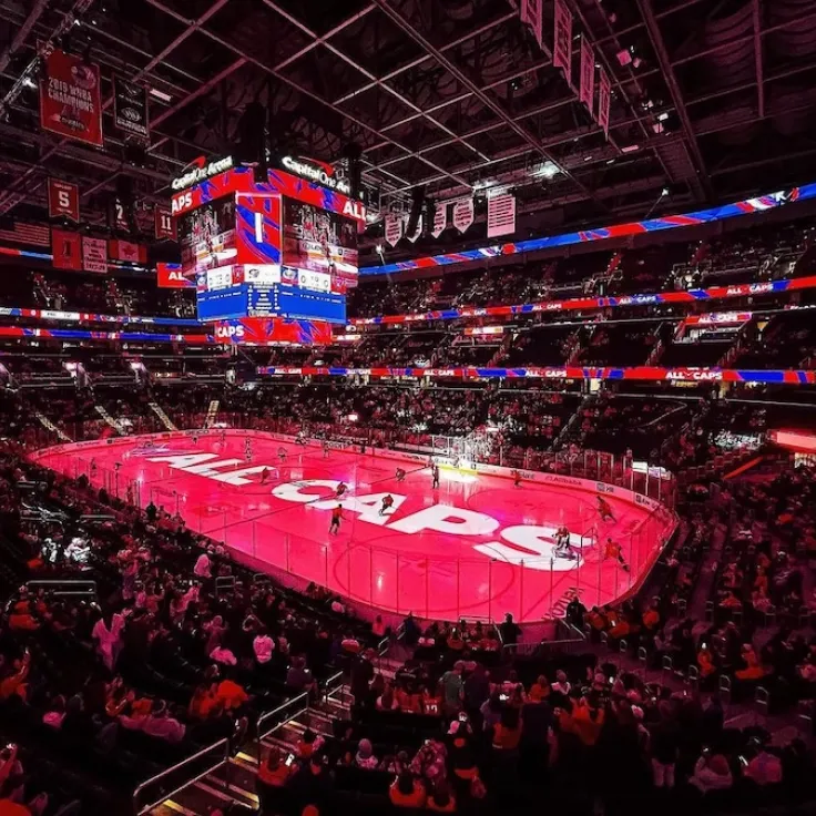 Photo of a packed arena during an ice hockey game, with a bright red-lit rink and jumbotron