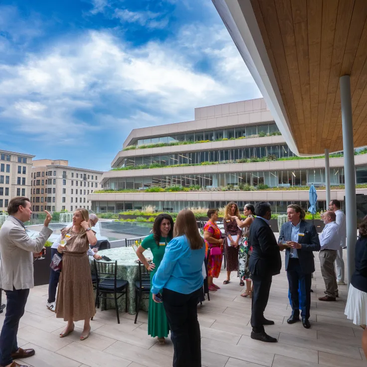 People mingle on rooftop terrace beside modern building under cloudy sky