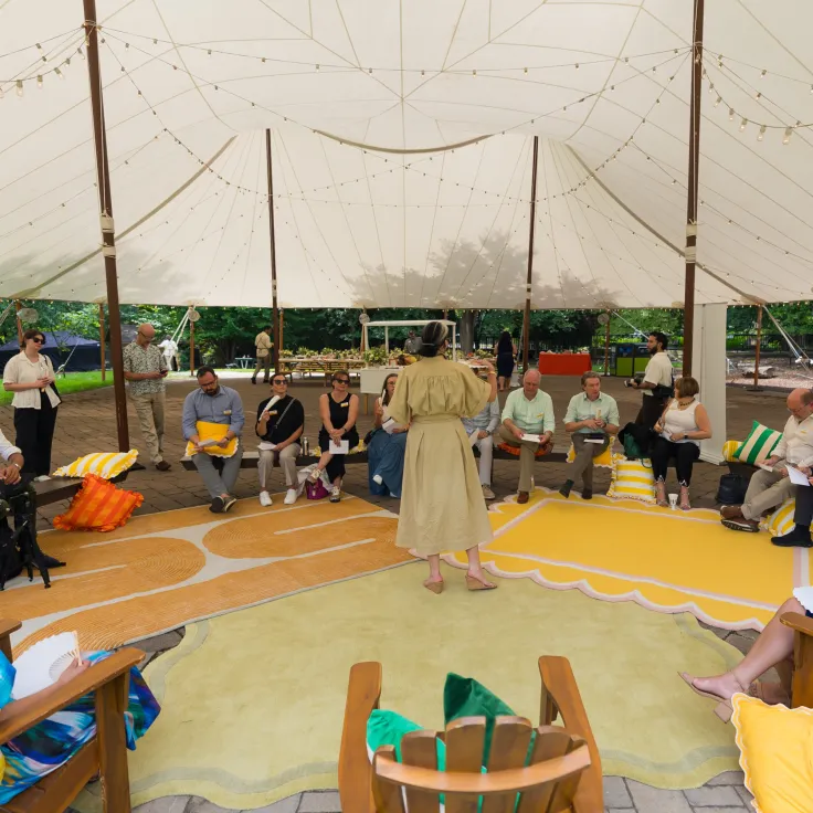 People in a circle under a canopy tent as a speaker leads an outdoor workshop