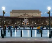 People ice skating at the National Gallery of Art Sculpture Garden rink during the evening, with string lights overhead and the museum building in the background.