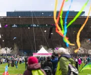 A colorful scene from the Blossom Kite Festival with kites flying in the sky in front of the National Museum of African American History and Culture.