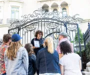 A tour guide speaks to a group outside of an ornate gate to a DC embassy. 