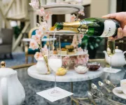 A hand pours champagne into a glass on a table set for a lavish high tea. 