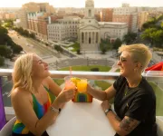 A couple enjoying a cocktail on a rooftop with a view of historic city buildings below. 