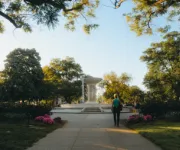 A scenic view of Dupont Circle featuring the central fountain, blooming flowers, and people strolling along the sunlit pathways.
