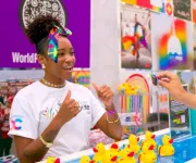 A young woman with a rainbow bow in her hair plays a game with an attendee at an event booth.