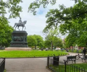 A wide view of Logan Circle Park featuring a large equestrian statue surrounded by leafy trees and benches on a sunny day.