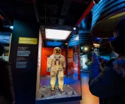 A visitor takes a photo of Neil Armstrong’s Apollo 11 spacesuit on display behind glass.