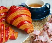 A table with quiche, sandwich, raspberry croissant, dessert, cherries and coffee.