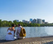 A couple sits by the Georgetown waterfront, looking out across the Potomac River toward the skyline of Rosslyn, Virginia.