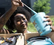 An artist dips a brush into a container of brightly colored paint. 
