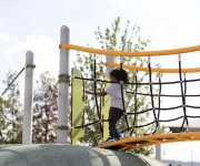 A young child climbs across a rope bridge on a colorful playground structure in Washington, DC.