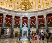 Visitors stand beneath the ornate dome and red curtains of the National Statuary Hall inside the U.S. Capitol.