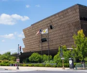 A view of the National Museum of African American History and Culture on a sunny day as cars pass by. . 