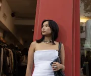 Woman in strapless white top standing by red doorway, looking left