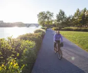 Cyclist on a riverside path at sunset, with trees and green grass nearby