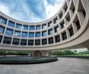 Curved modern building with large windows surrounding a circular fountain under blue sky