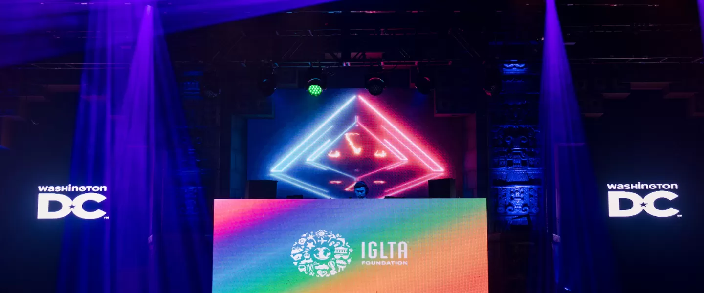 A colorful stage setup with vibrant lighting and LED screens displays logos for Washington D.C. and the IGLTA Foundation.