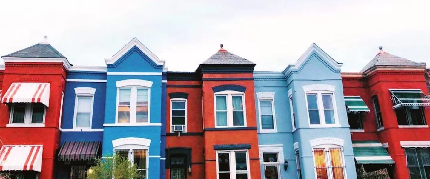 A row of colorful townhouses with red, blue, and light blue facades and striped awnings in Washington, D.C.