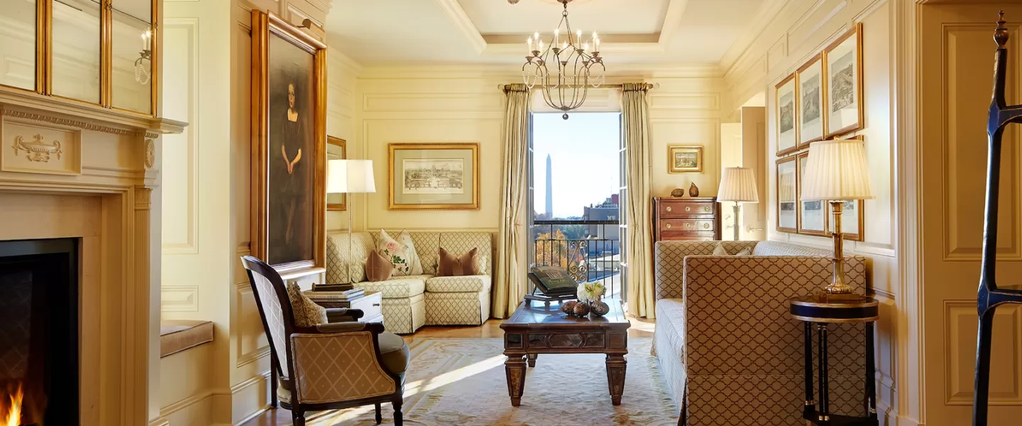 A luxurious living room with a fireplace, chandelier, and a mix of classic and modern furniture. The room features a large window with a view of the city and a warm, inviting color palette.