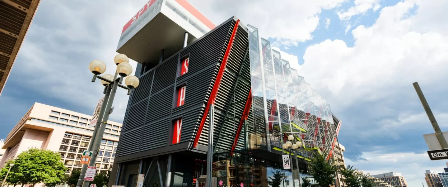 O exterior moderno do Museu Internacional da Espionagem em Washington, DC, apresentando um design marcante com detalhes em vermelho e painéis de vidro sob um céu nublado.