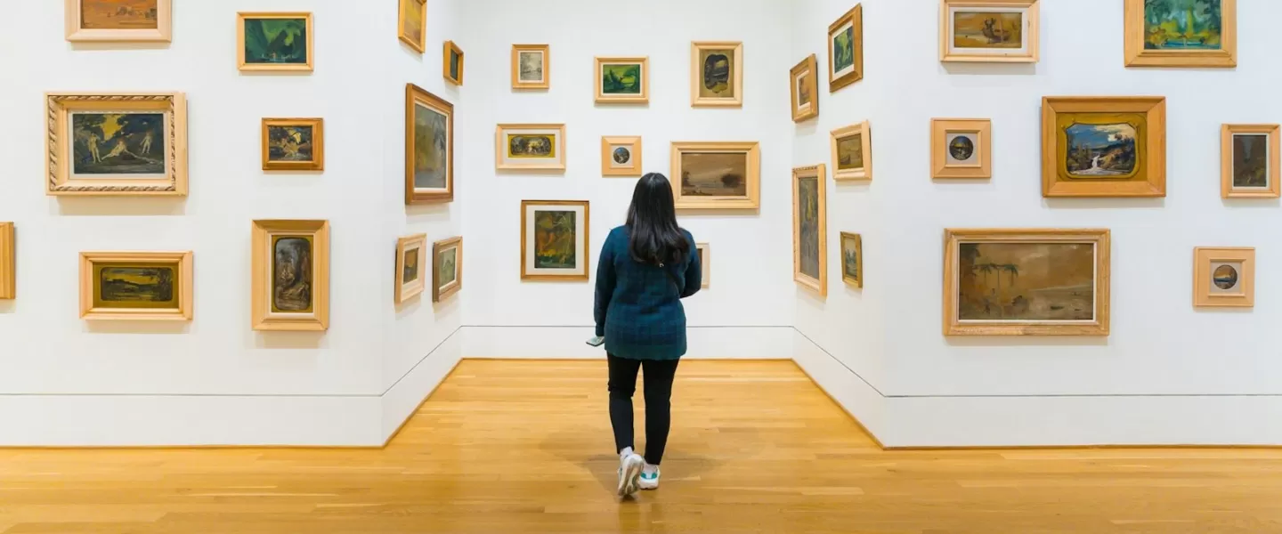Un visitatore esplora una galleria della Phillips Collection, dove piccoli dipinti incorniciati in vari stili sono disposti su pareti bianche, creando un'esperienza artistica immersiva.