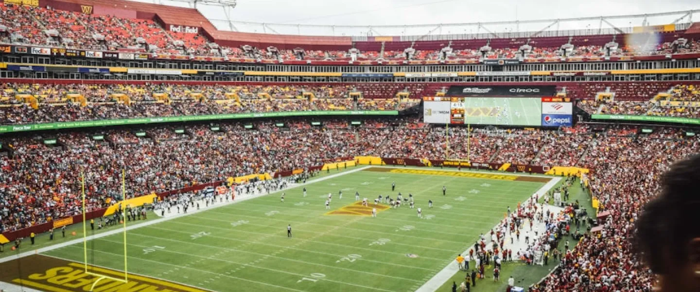 A packed stadium during a Washington Commanders football game, with fans filling the stands and players on the field at FedExField.