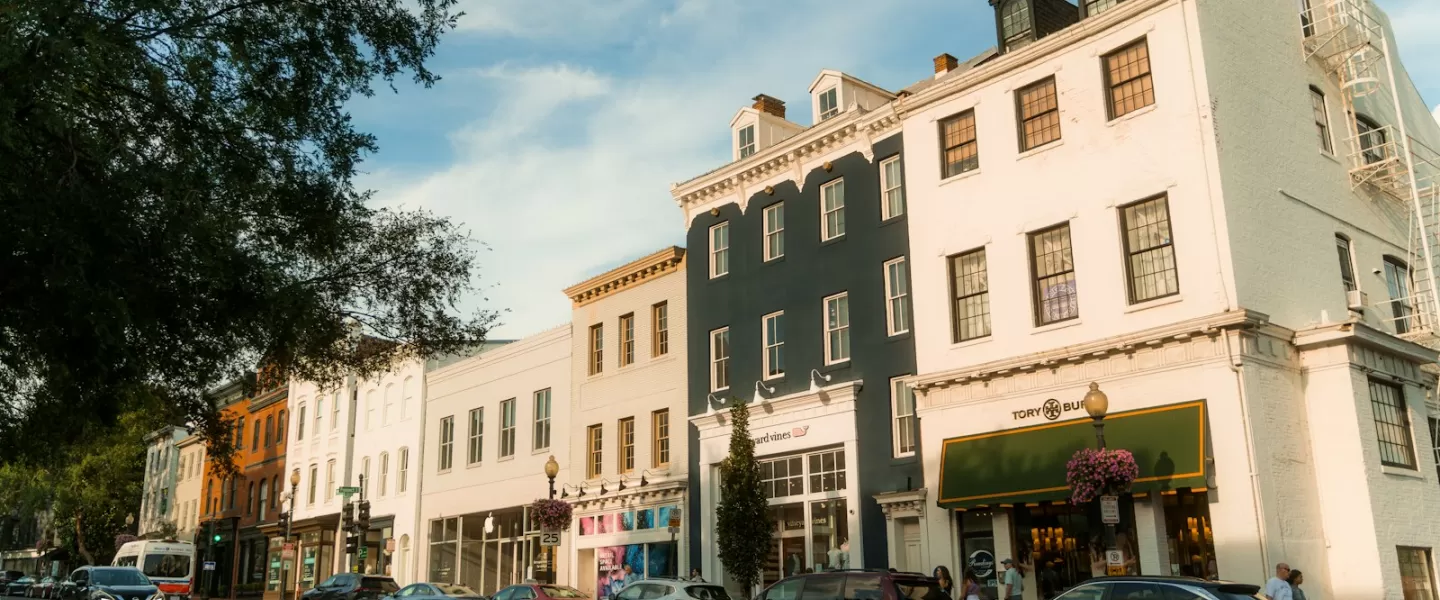 Un pintoresco paisaje urbano de Georgetown con encantadores edificios históricos con tiendas boutique y autos estacionados, bañados por la luz del sol del atardecer bajo un cielo despejado.