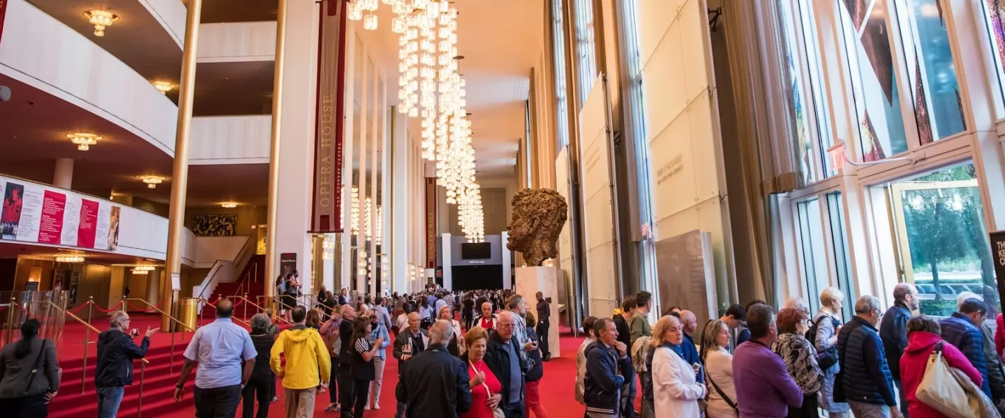 Eine überfüllte Lobby im Kennedy Center, in der Menschen an einer großen Skulptur und Kronleuchtern unter einer hohen Decke vorbeigehen.