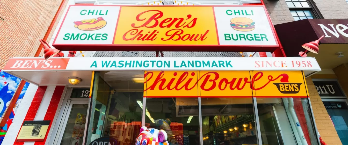 A icônica fachada do Ben's Chili Bowl em Washington, DC, com uma vibrante placa vermelha, amarela e branca que diz "Ben's Chili Bowl, um marco de Washington desde 1958".