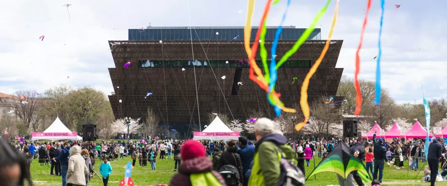 Una escena colorida del Blossom Kite Festival con cometas volando en el cielo frente al Museo Nacional de Historia y Cultura Afroamericana.
