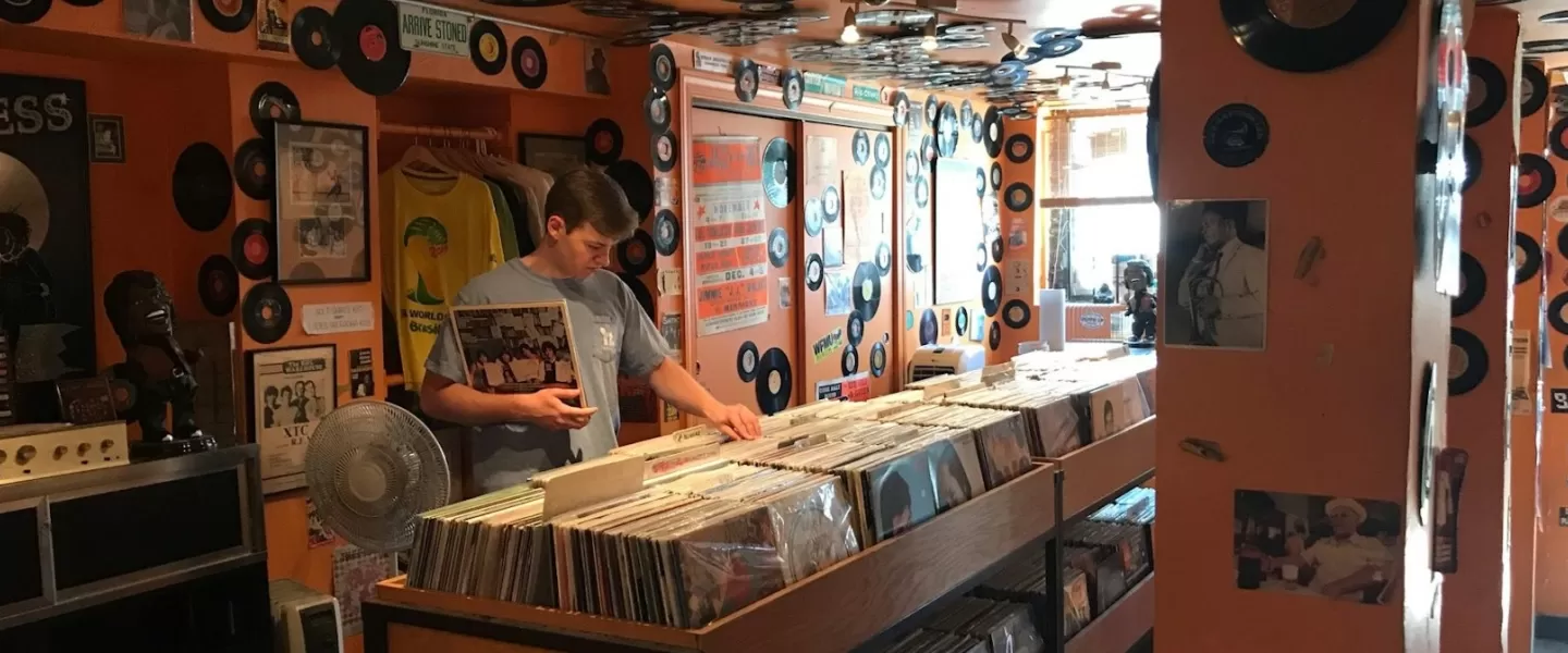 Um cliente olha discos de vinil em uma loja colorida, decorada com discos e folhetos.