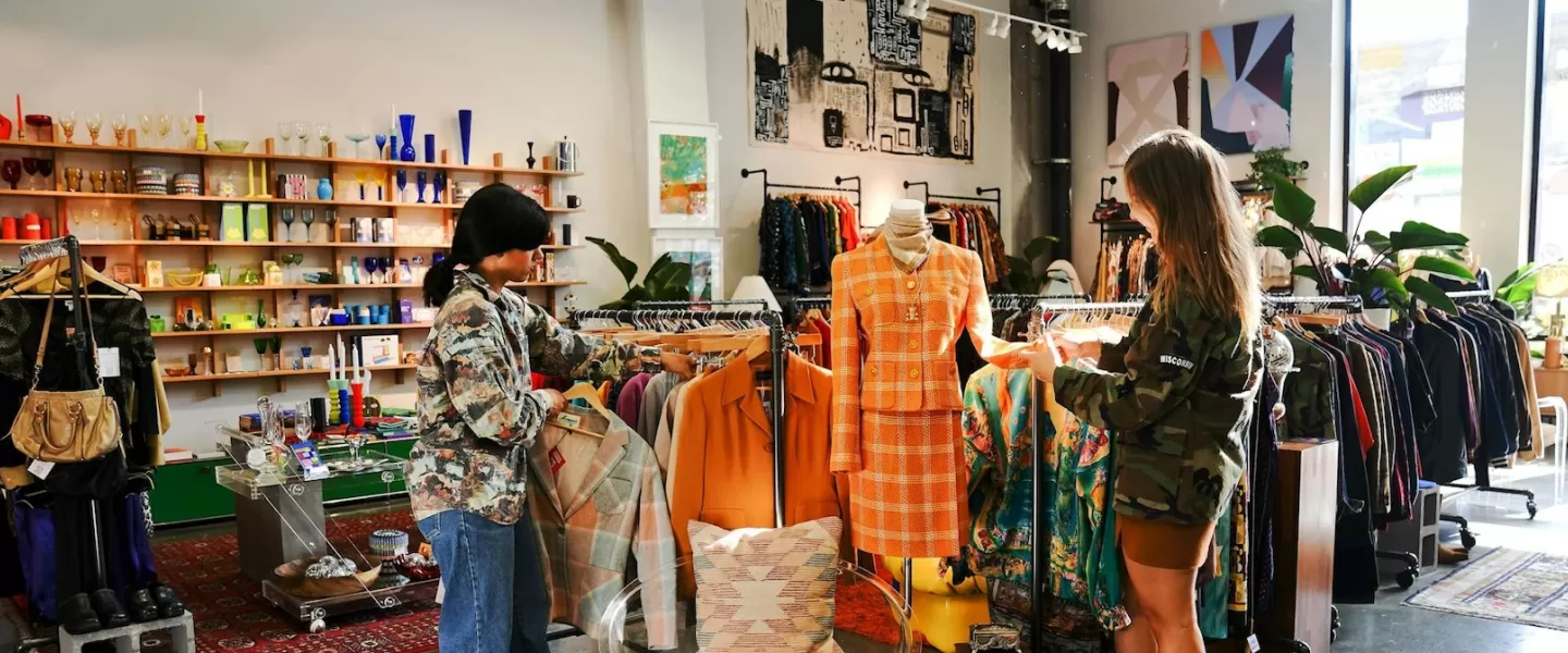 Due clienti esplorano un negozio vintage ben curato, pieno di articoli di moda e arredamento unici.