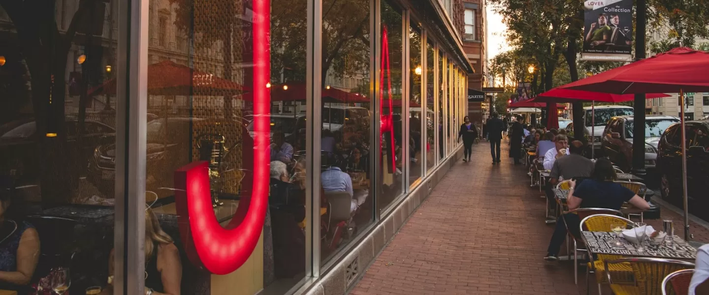 O exterior do Jaleo by José Andrés em Washington, DC, com grandes letras vermelhas em neon e mesas ao ar livre sob guarda-sóis vermelhos.