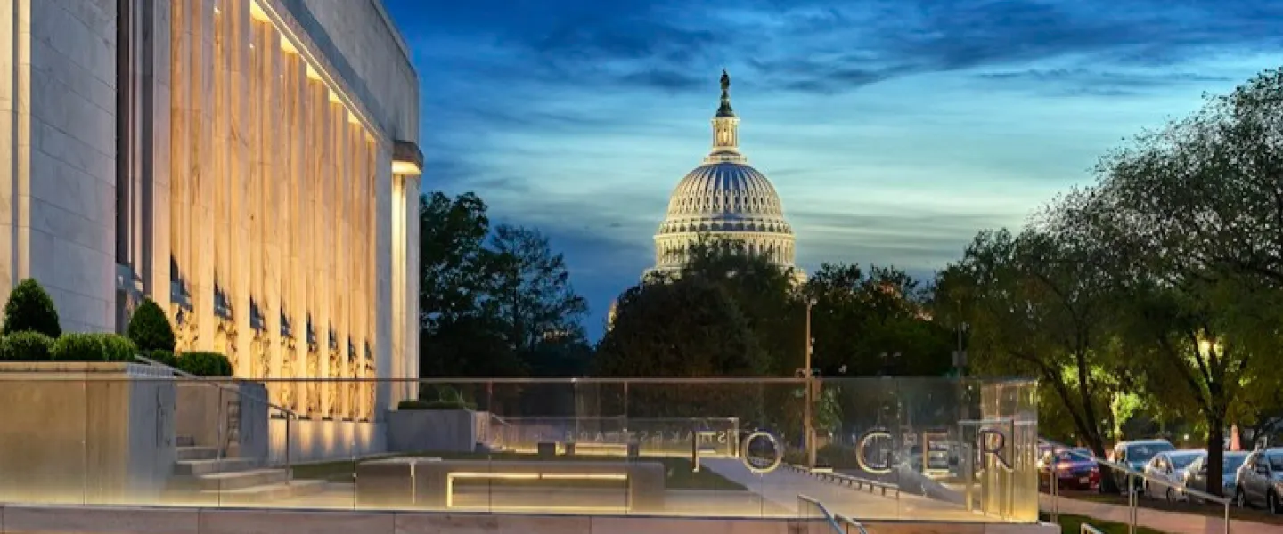 The illuminated exterior of the Folger Shakespeare Library at dusk, with the U.S. Capitol visible in the background.