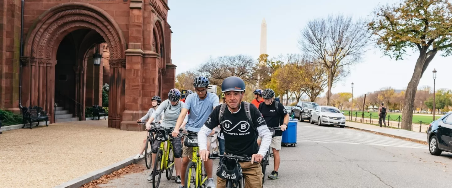 Um guia lidera um passeio de bicicleta pelo National Mall com o Castelo Smithsonian e o Monumento a Washington ao fundo.