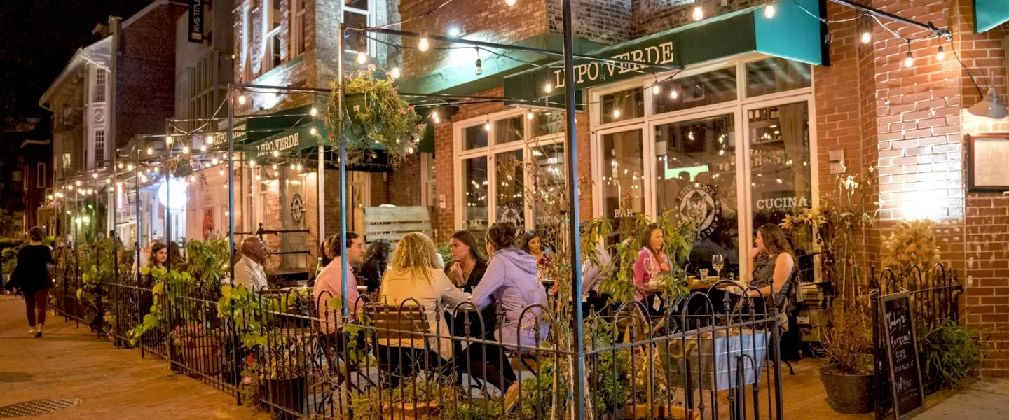 Diners enjoy a cozy evening meal under string lights on the outdoor patio of Lupo Verde along 14th Street.