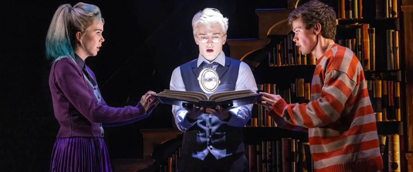 Three characters intensely examine a glowing magical object in a dramatic scene from Harry Potter and the Cursed Child.