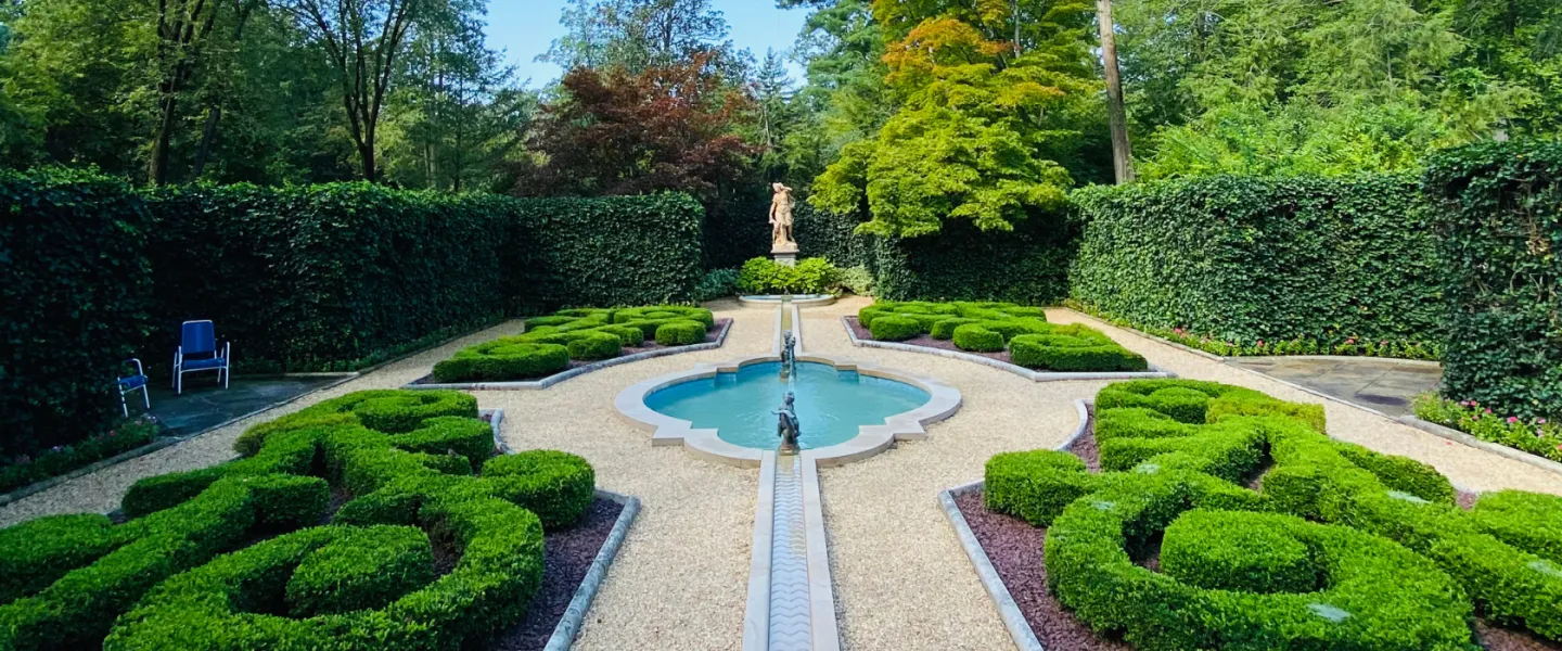 Formal garden with sculpted boxwood hedges, a central fountain, and a classical statue surrounded by tall green hedges in Washington, DC.
