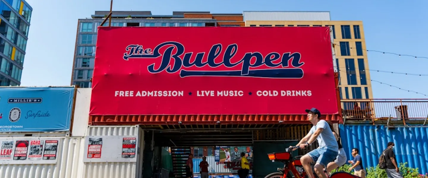 A cyclist rides past The Bullpen, an open-air venue near Nationals Park advertising live music, cold drinks and free admission.