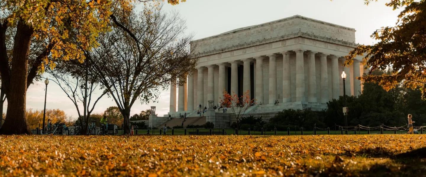 The Lincoln Memorial framed by fall foliage, with leaves coverage the grass in orange and yellow hues.
