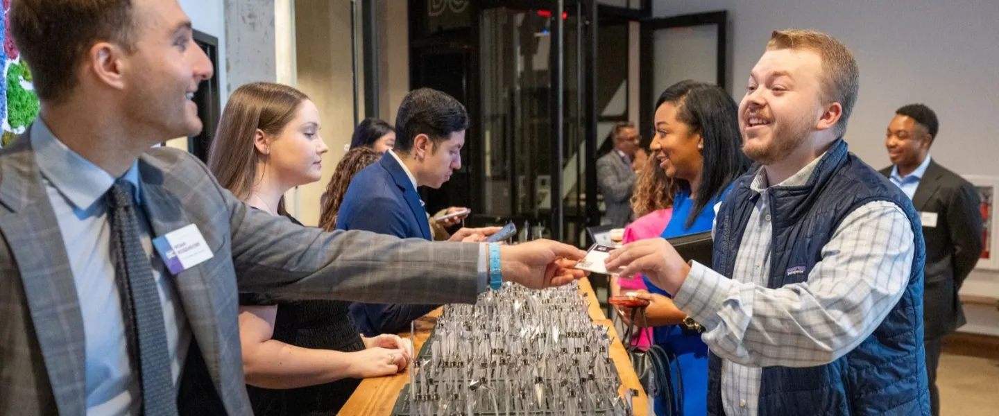 A man smiles as he receives a name badge at an event check-in table staffed by several people.