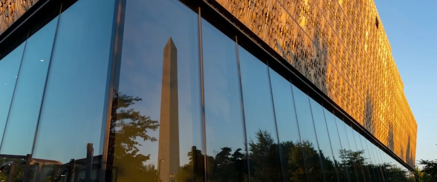 The Washington Monument reflected in the glass exterior of the National Museum of African American History and Culture at sunset.