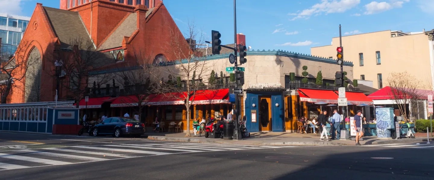 People dine outside under red awnings at Le Diplomate on a sunny day in Washington, DC.